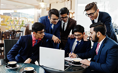 A group of young men in suits and ties collaborating on a laptop.