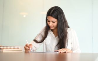 A woman focusedly writes on a piece of paper, pen in hand, as she expresses her thoughts and ideas.