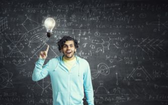 A man holding a light bulb in front of a blackboard, symbolizing creativity and innovation.