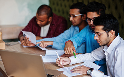 A diverse group of individuals sitting around a table with laptops, engaged in a meeting or collaboration.