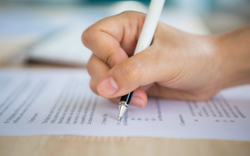 a hand holding a pen writes on a paper, creating words and lines