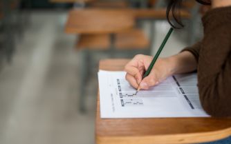 a woman focusedly writes on paper at a desk displaying determination and concentration in her work