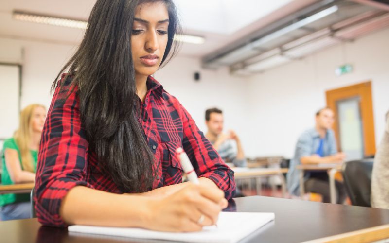 a woman in a classroom focused on writing on a piece of paper