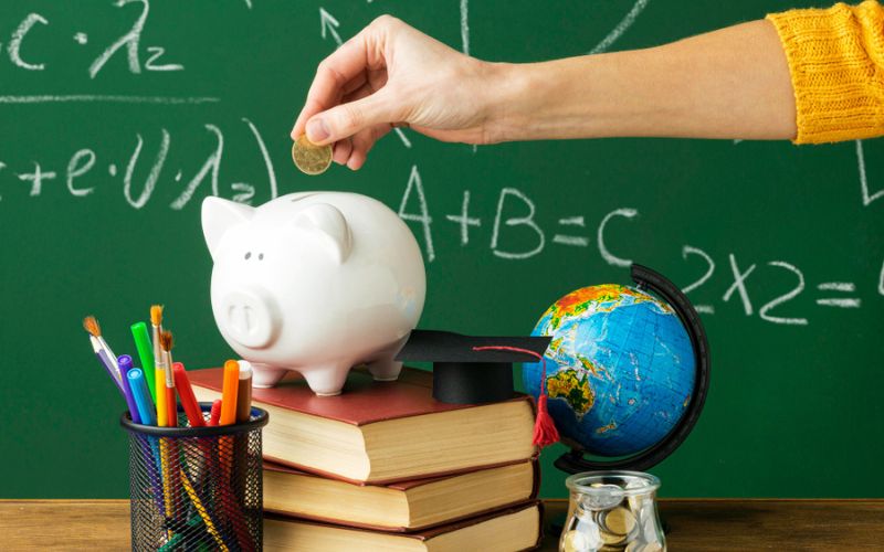 A piggy bank filled with coins and books placed on a blackboard.