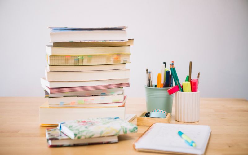 a neat desk with a stack of books, pens, and a notebook