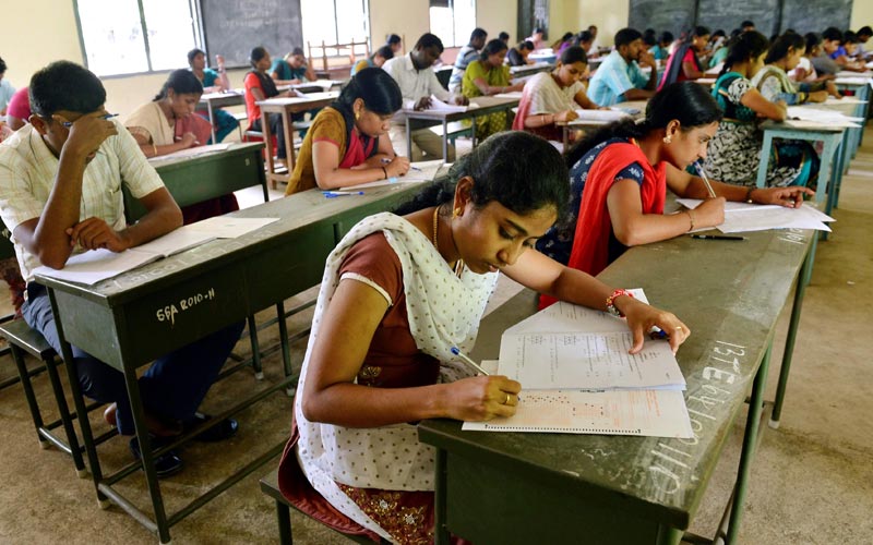 A diverse group of individuals sitting at desks in a classroom, giving government job exam.