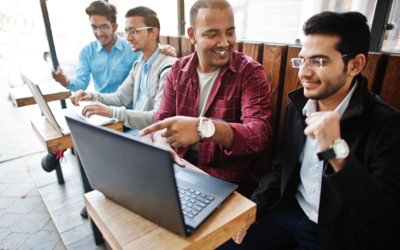 group four indian teen male students classmates spend time together work laptops