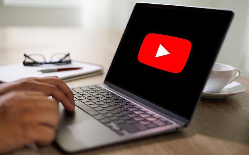 an image showing a laptop with a hand and YouTube on the screen