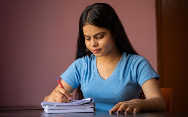 a young woman focused on writing in a notebook while sitting at a table