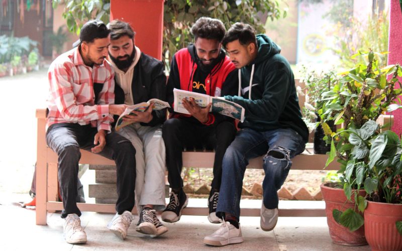Four young men engrossed in a book while sitting on a bench
