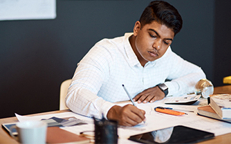 a man sitting at a table, working on a laptop and surrounded by papers.