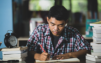 A woman in a red shirt attentively sits in front of a classroom, engaged in a learning environment.